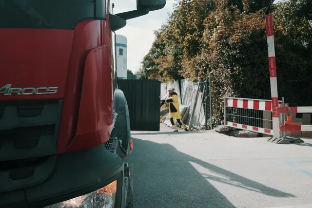 La cabine d’un camion M. Ducret SA à l’entrée d’un chantier, barrières rouges et blanches et ouvrier en gilet jaune au fond, image extraite du film Nereva